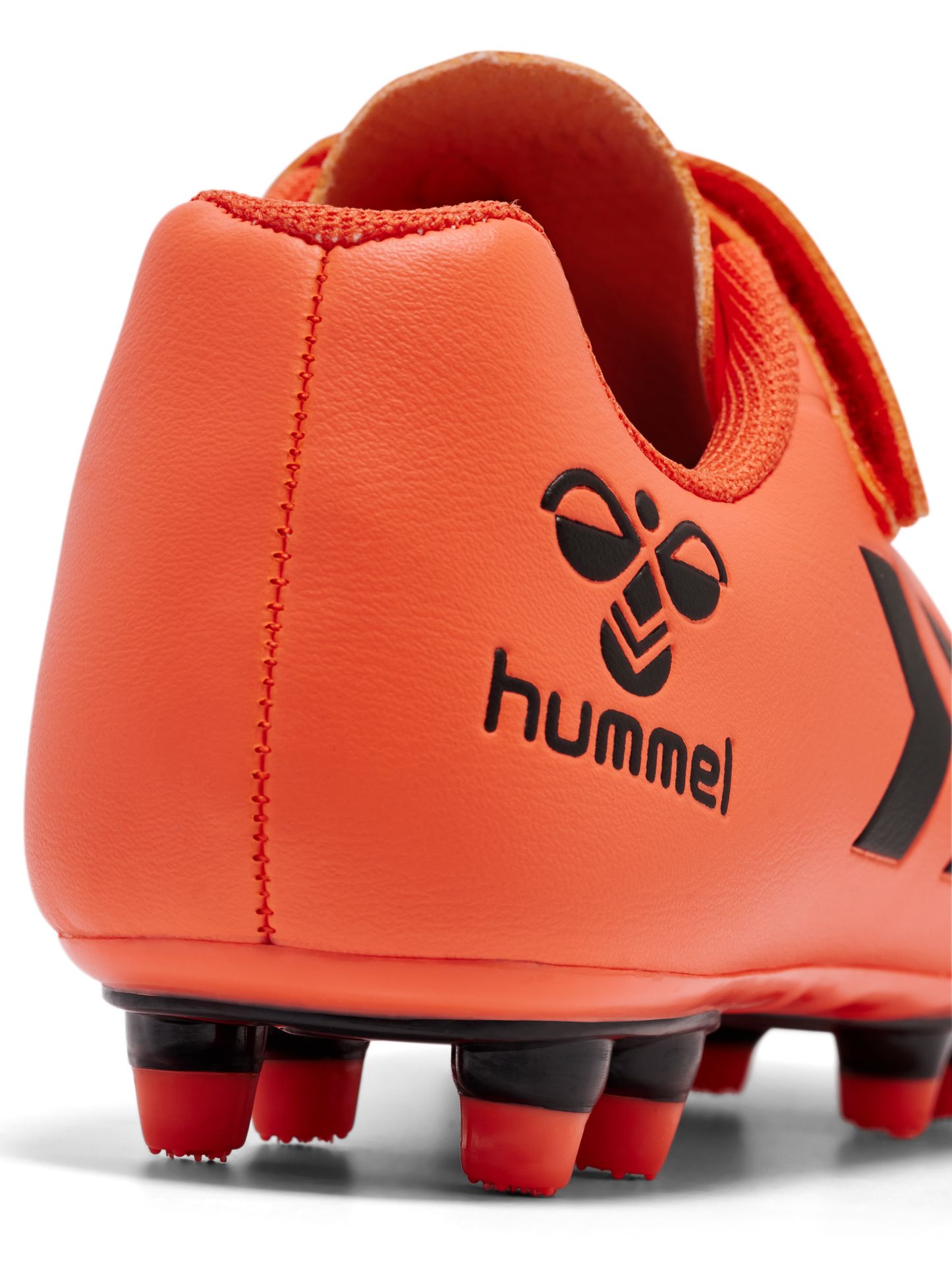 A football boot by Hummel, style Top Star F.G JR 216568-4127, in orange with black logo and velcro fastening. Close up of heel showing black Hummel logo.