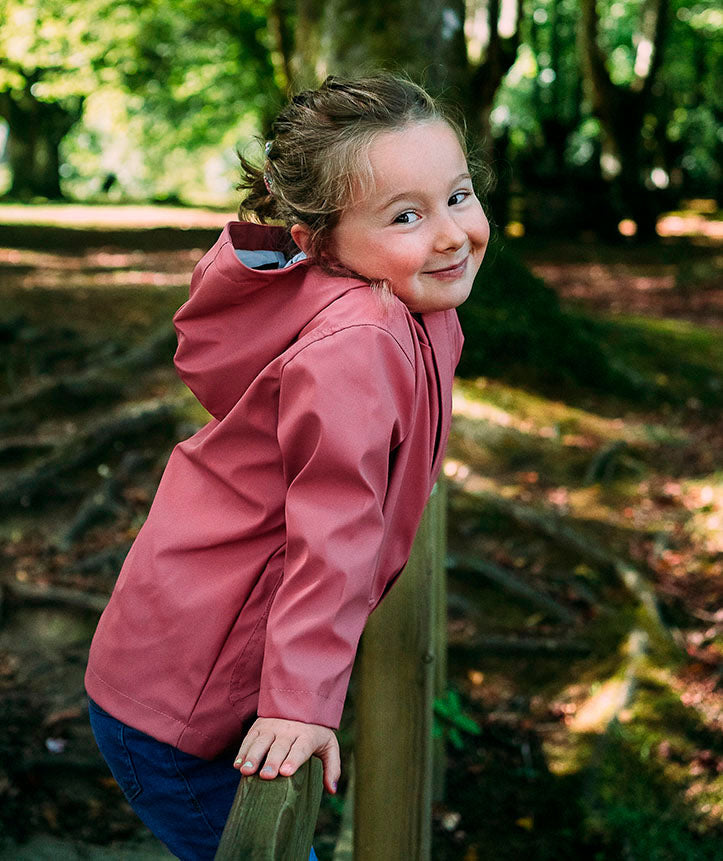 A girls hooded rain coat by Igor, style Euri, in pink with pockets and navy and white stripe lining. Lifestyle image.