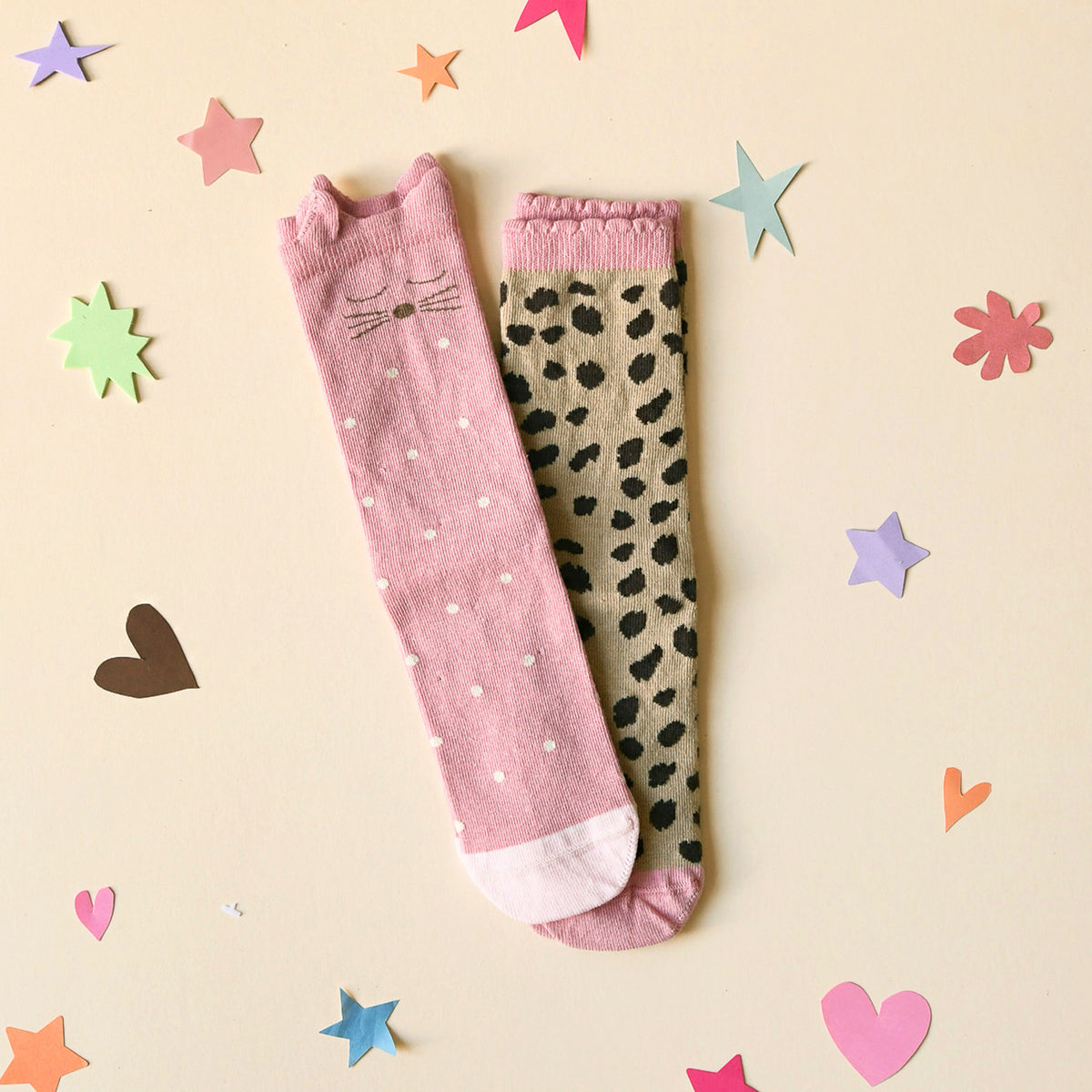 Two pairs of children's socks, one with pink cat design and one leopard print. Shown on background of colourful stars and heart shapes