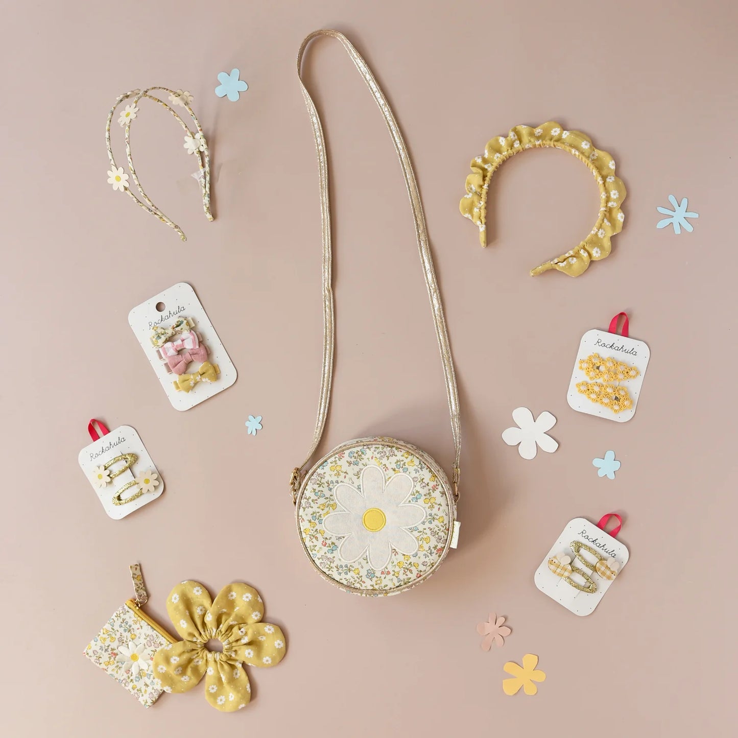 A selection of floral yellow and white accessories by Rockahula including bag, headband, hair clips and bobbles on a light pink background with flower confetti