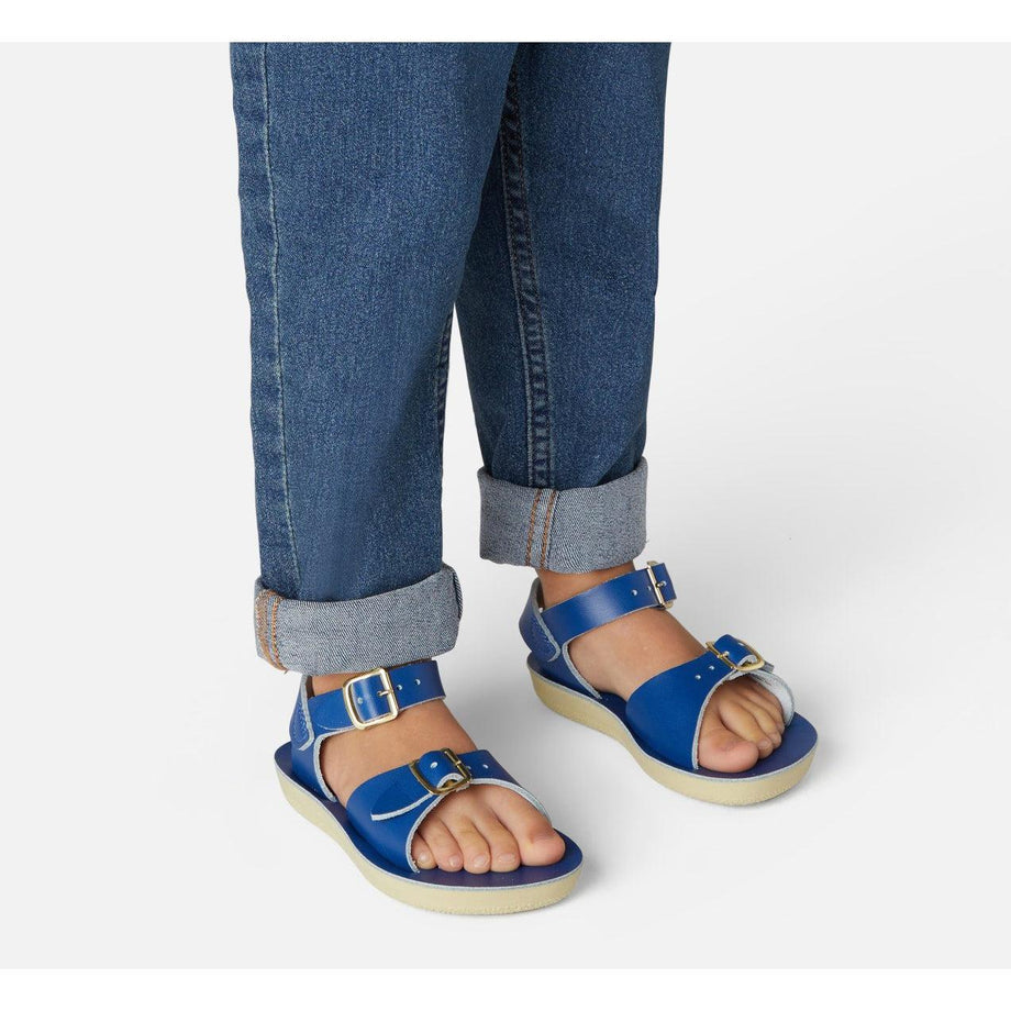 A unisex sandal by Salt Water Sandals in blue with double buckle fastening across the instep and around the ankle. Open Toe and Sling-back. Lifestyle of standing up view.