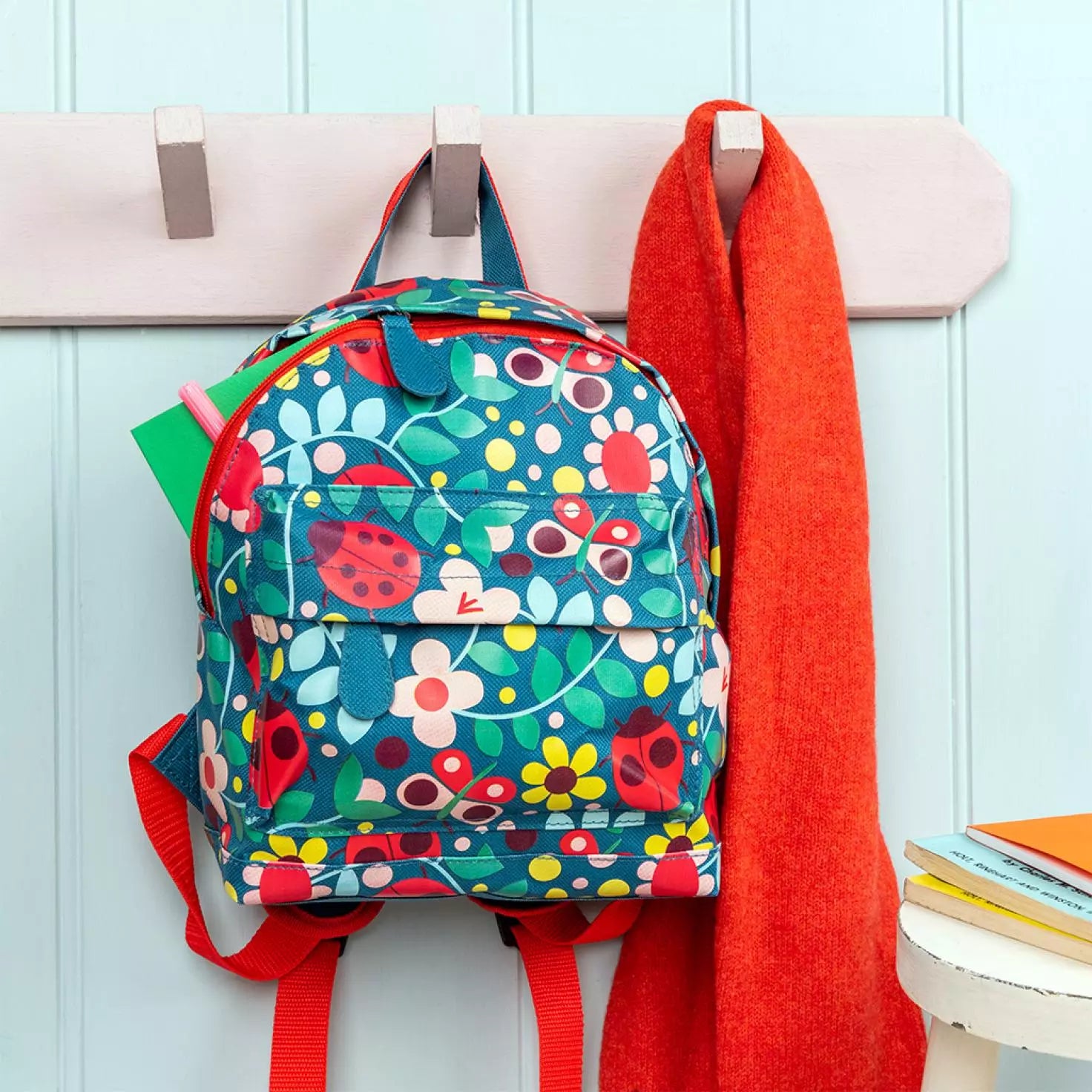 A childs backpack by Rex London, style Ladybird, in blue with multi ladybird and floral print. Two compartments with zip fastening. Lifestyle image.