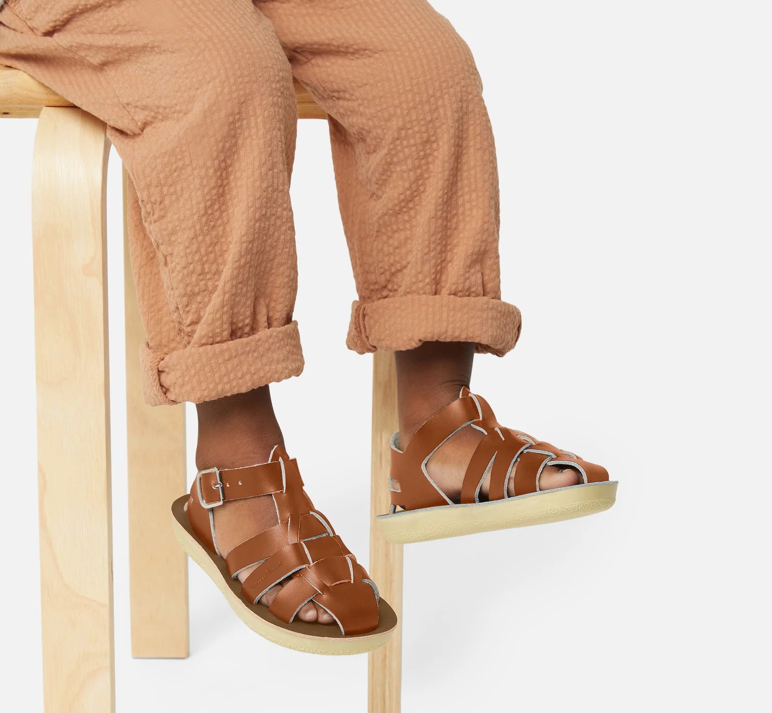 A unisex sandal by Saltwater, style Shark in tan with buckle strap. Image of childs legs wearing the sandals