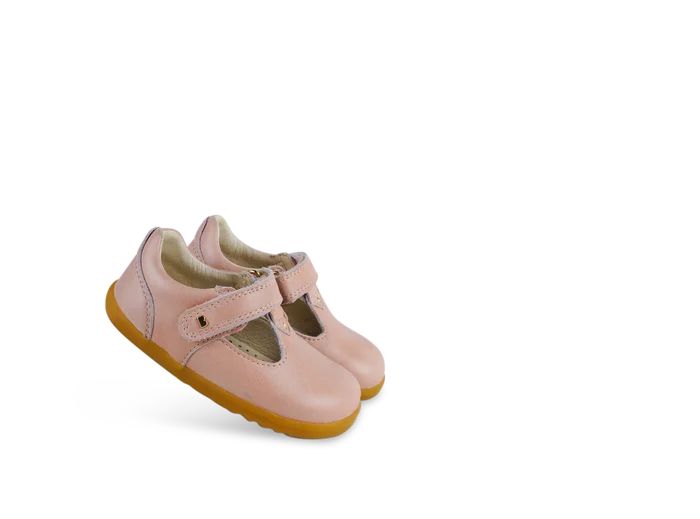 A girls first shoe by Bobux, style Louise, a velcro T-bar in dusky pink pearl. Angled view of a pair.