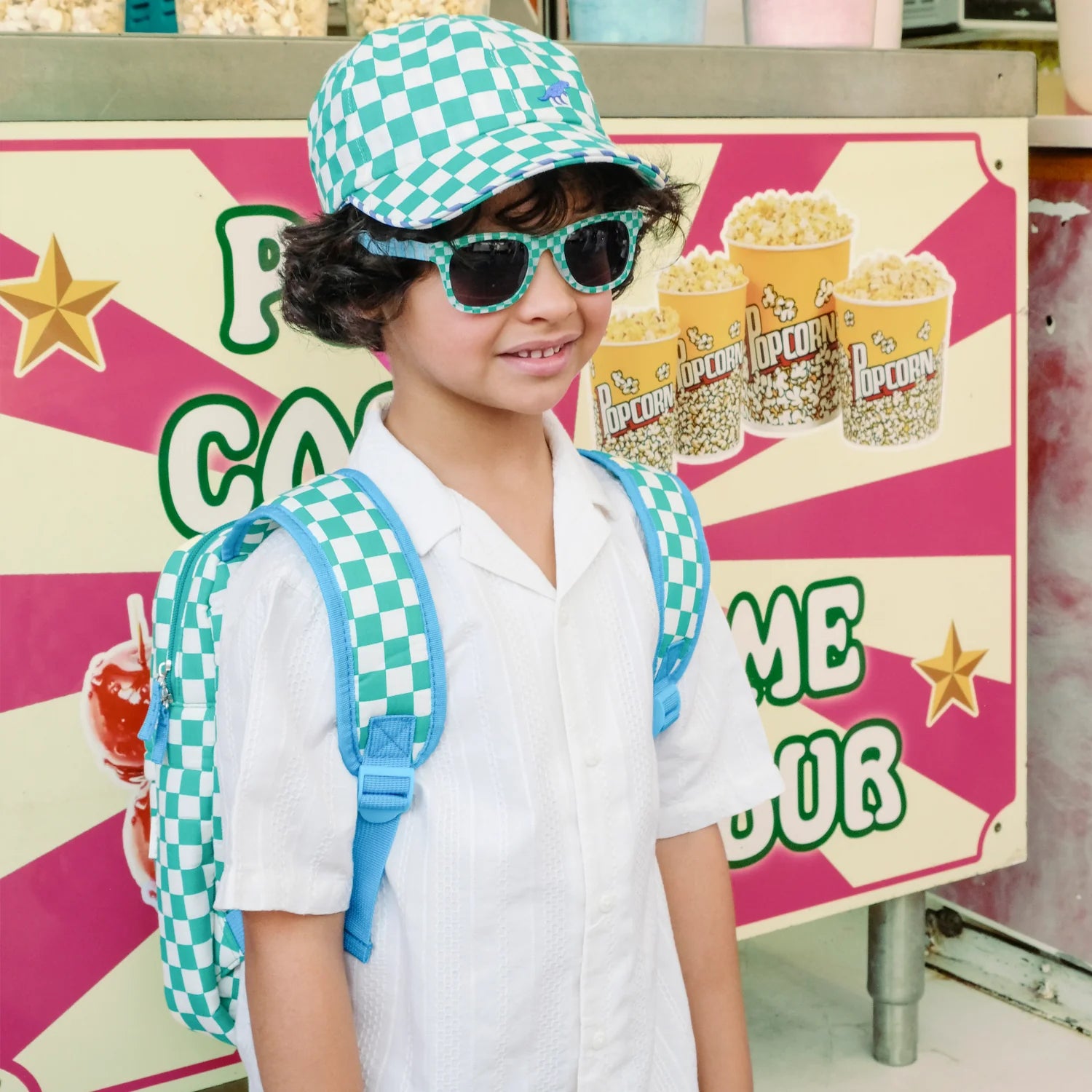 A boy wearing green and white check backpack, sunglasses and cap by Rockahula