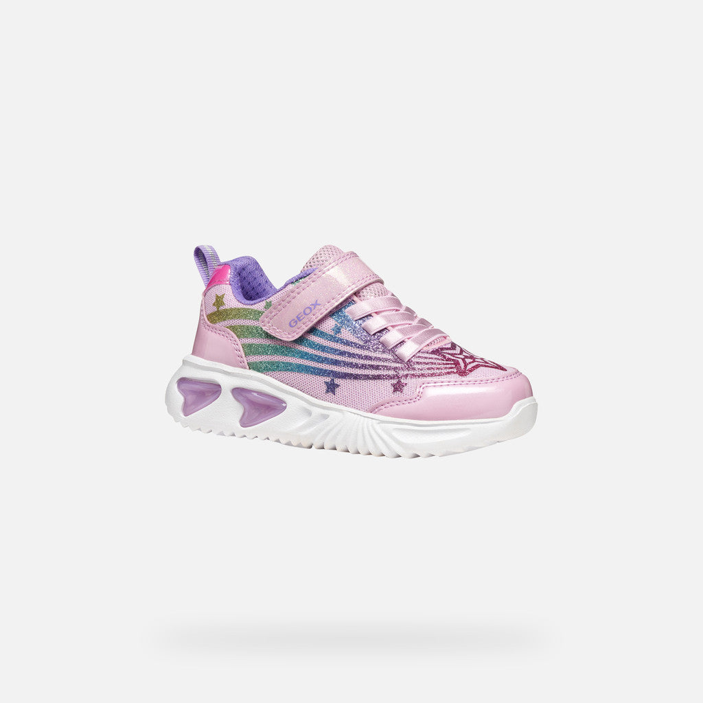 A pink girls trainer by Skechers, style Assister, in pink/multicolour with glittery rainbow and star design, velcro strap and pink laces. Angled side view