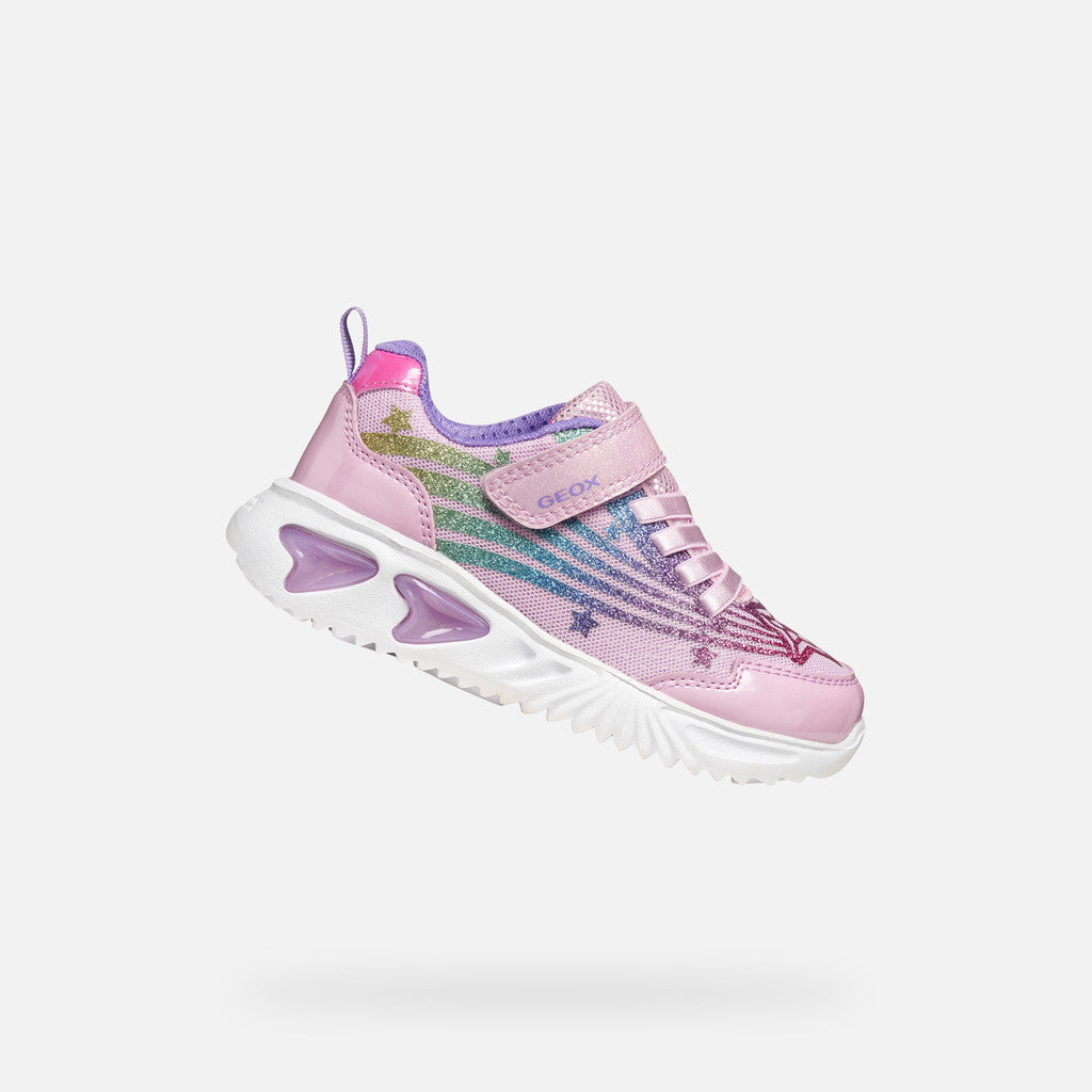 A pink girls trainer by Skechers, style Assister, in pink/multicolour with glittery rainbow and star design, velcro strap and pink laces. Lifted right side view