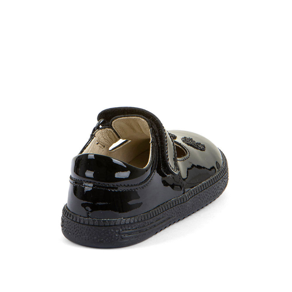 A girls barefoot school shoe by Froddo. In a loop Sandra style, black patent, with a tbar velcro strap and love heart design on the front. Angled back view.