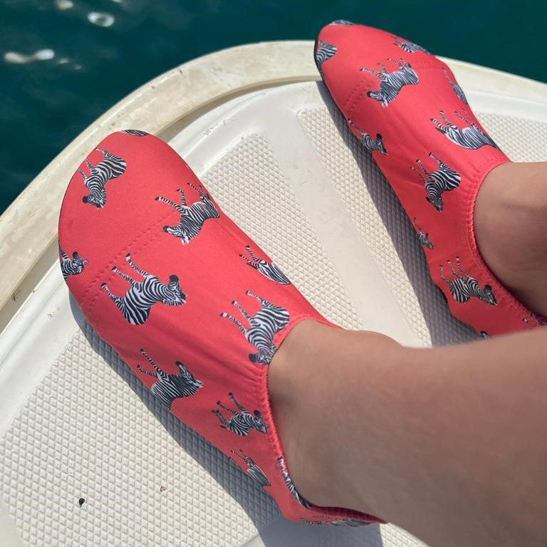 A unisex non slip swim shoe by Slipfree, style Grevy, in coral with Zebra print. Lifestyle image.