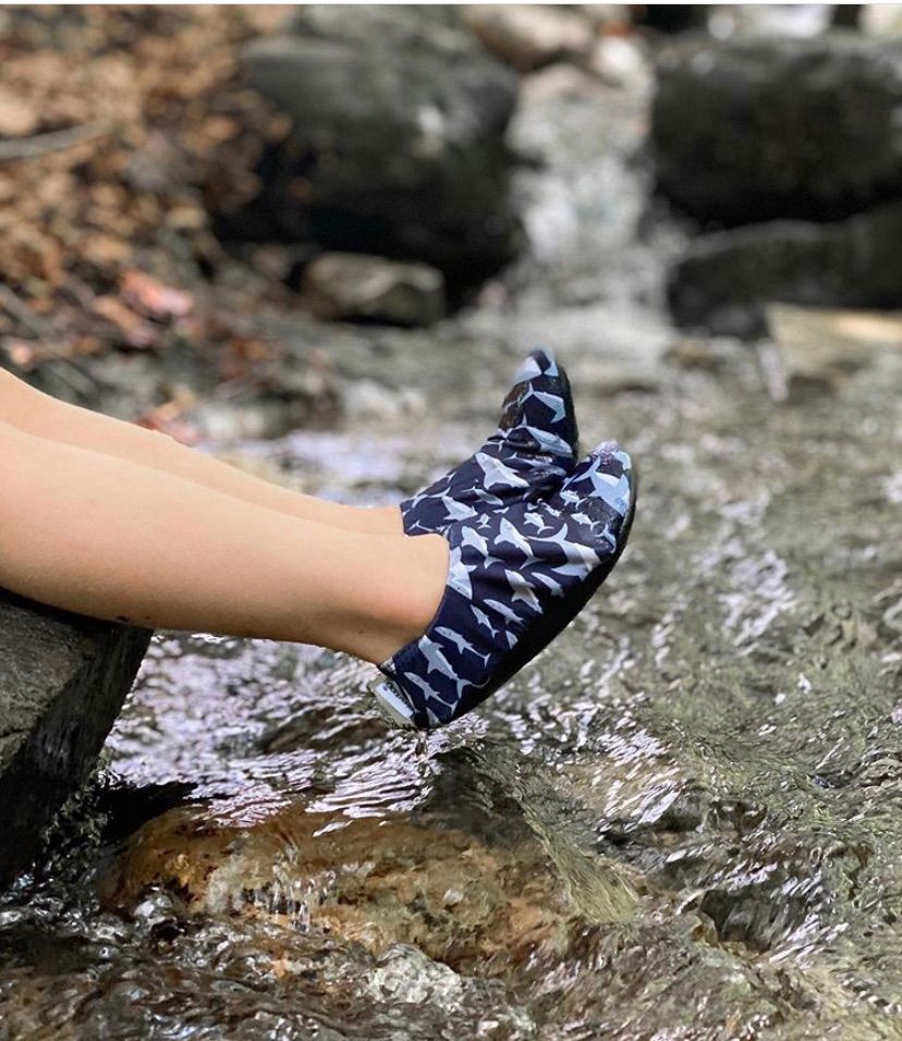 Childs feet in a river, wearing a pair of boys non slip swim shoes by Slipfree, style Sharks, in navy with grey shark print. Right side view.