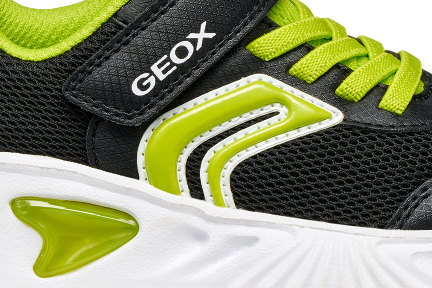 A boys trainer by Geox, style Assister, in black/lime with velcro strap and green laces. Close up view.