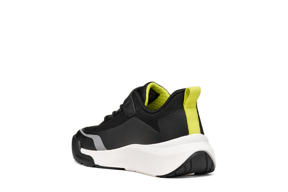 Geox boys trainer in the style Pro-Ran in black, white and grey with a Velcro strap, GEOX logo and white sole. Angled back view of right shoe. 