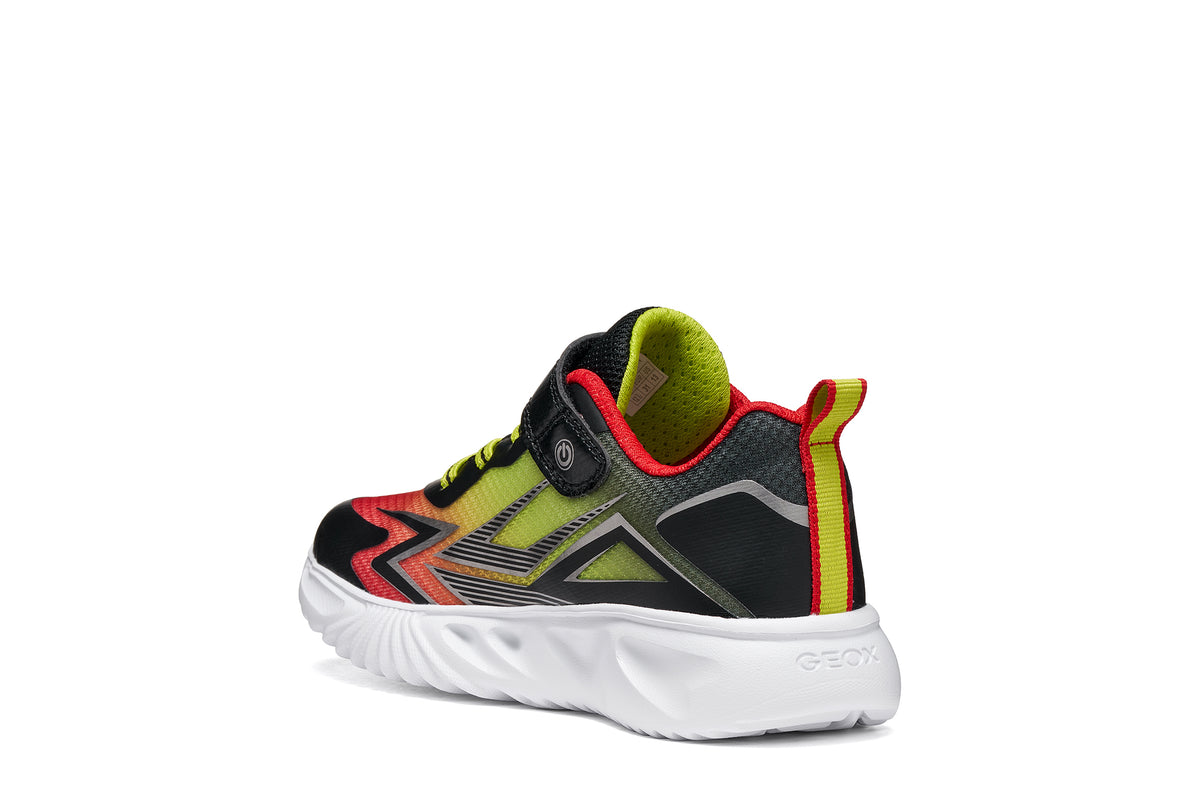 Geox boy's trainer in the style Assister, in red, yellow and black with a Velcro strap, lights and a white sole. Angled back view of right shoe. 