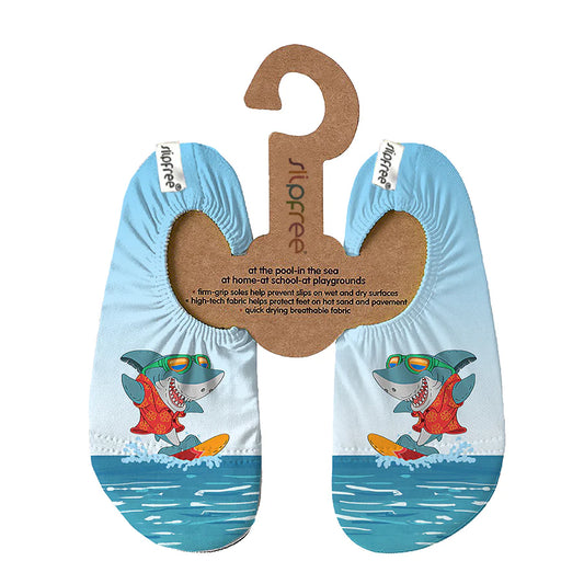 A pair of swim shoes by Slipfree, style Redd in blue with shark surfing cartoon design, hanging on cardboard hanger