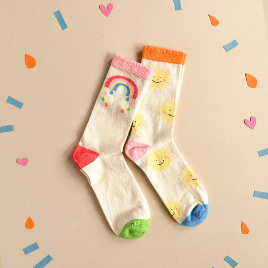 Pair of socks by Rockahula with colourful rainbow and sun designs on a beige background with confetti
