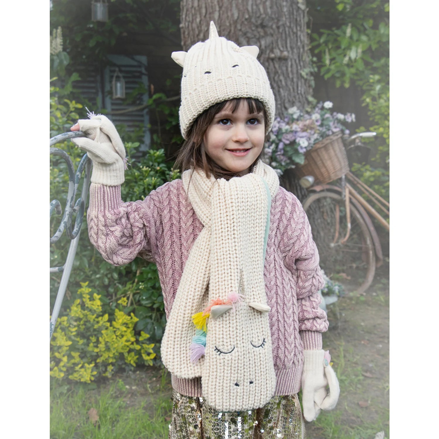A pair of knitted fingerless gloves by Rockahula, style Rainbow Unicorn M2230M  in cream with fleece lined buttoned finger cap and embroidered unicorn face. Lifestyle image.