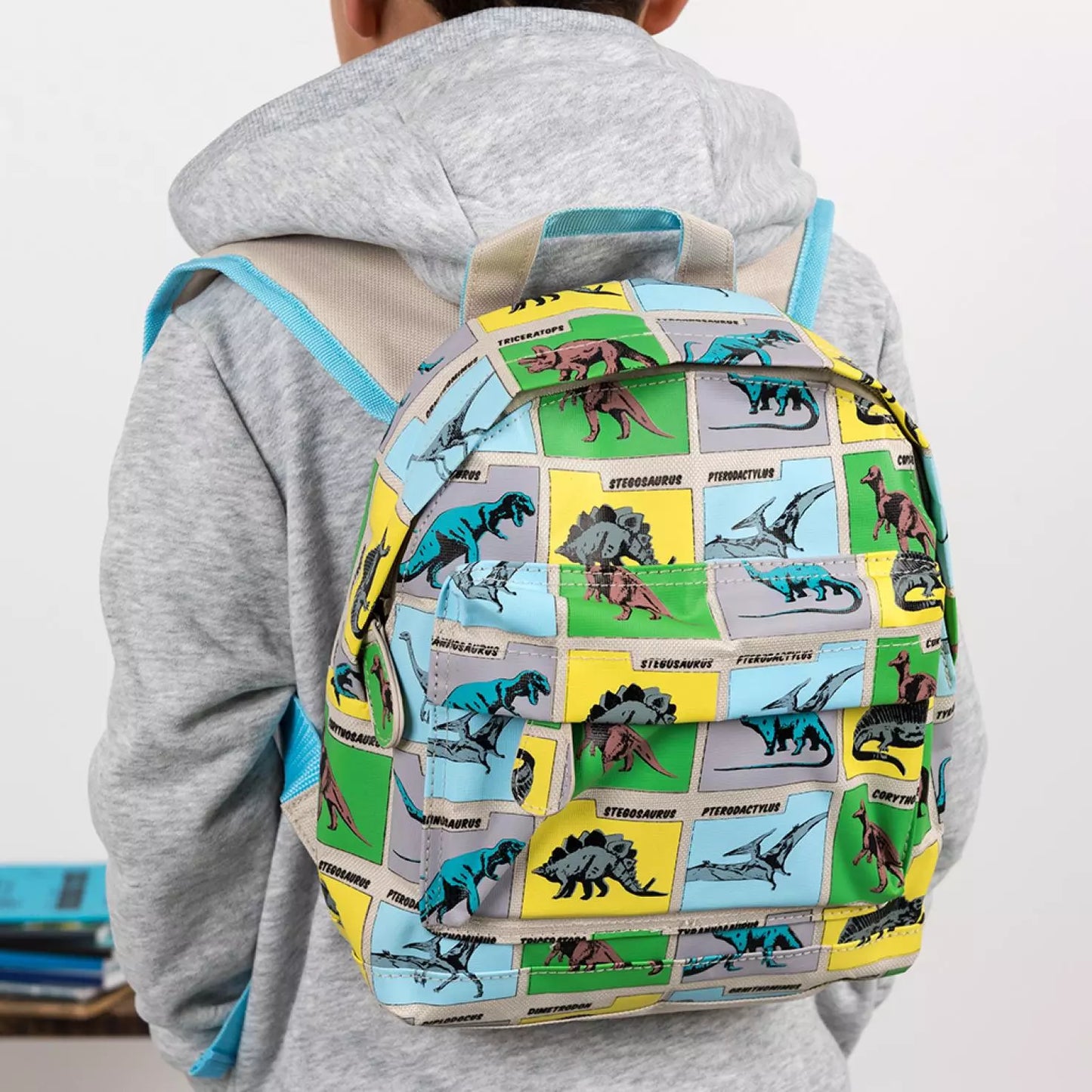 A childs backpack by Rex London, style Prehistoric Land, in blue, green and yellow multi dino print, two compartments with zip fastenings. Lifestyle image.