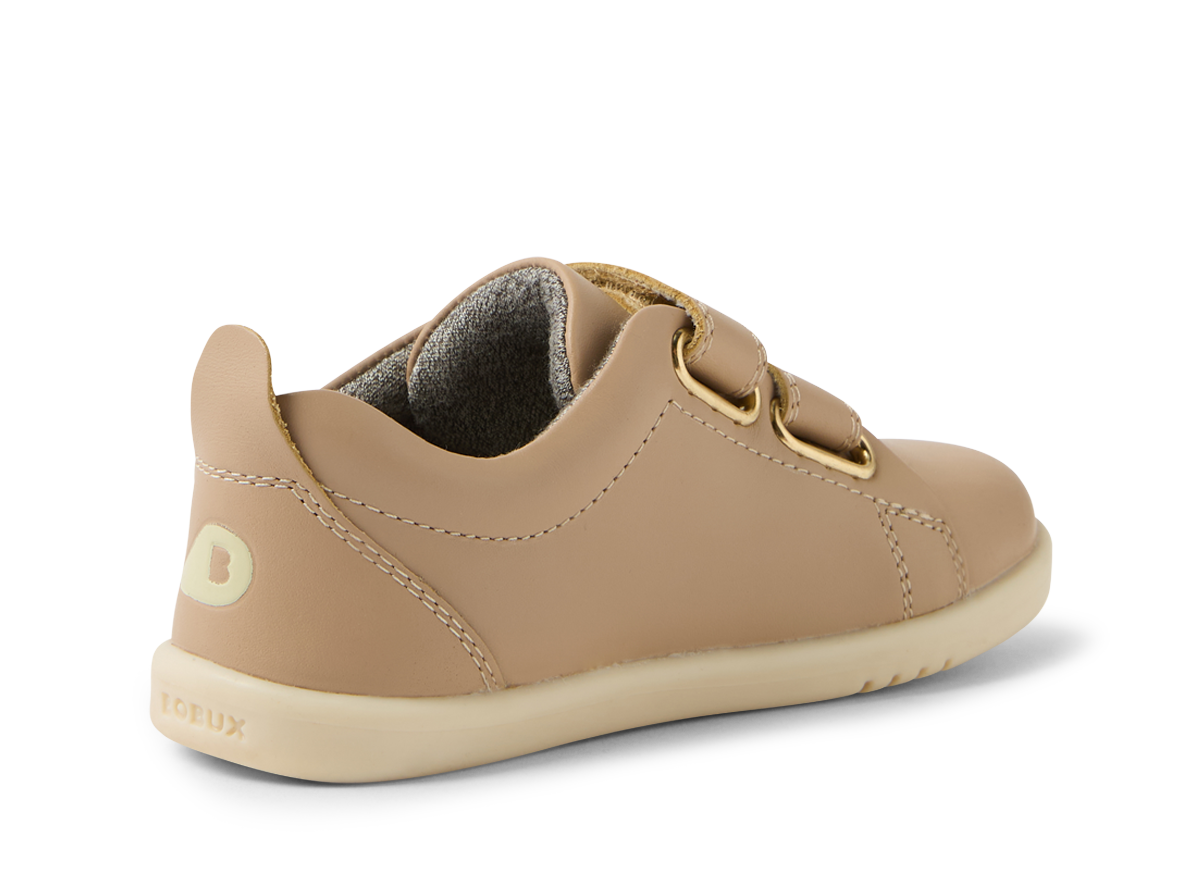 A unisex casual shoe by Bobux, style Grass Court, in taupe leather with double velcro fastening. Angled left side view showing Bobux logo.