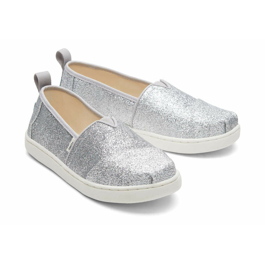 A girls canvas shoe by TOMS, style Alpargata, a slip on in silver glitter. Front view of a pair.