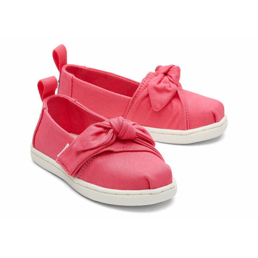 A girls canvas shoe by TOMS, style Alpargata Bow in the colour Pink Raspberry with velcro fastening.Top view of a pair.