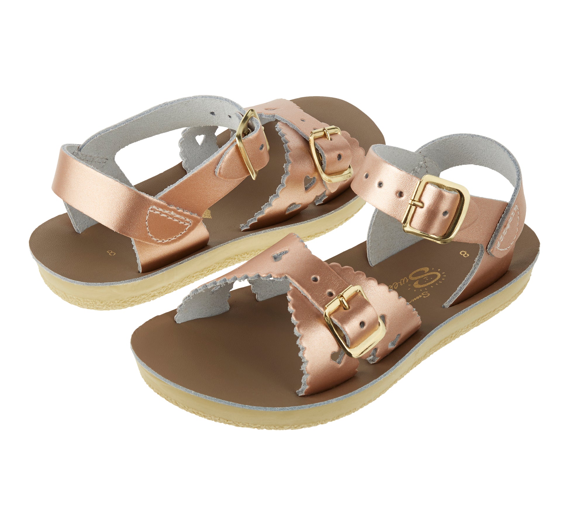 A girls sandal by Salt Water Sandal in rose gold with double buckle fastening across the instep and around the ankle. Featuring scallop edge and punched out heart detail. Side by side view.