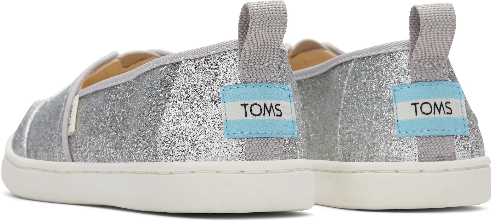 A girls canvas shoe by TOMS, style Alpargata, a slip on in silver glitter. Back view of a pair.
