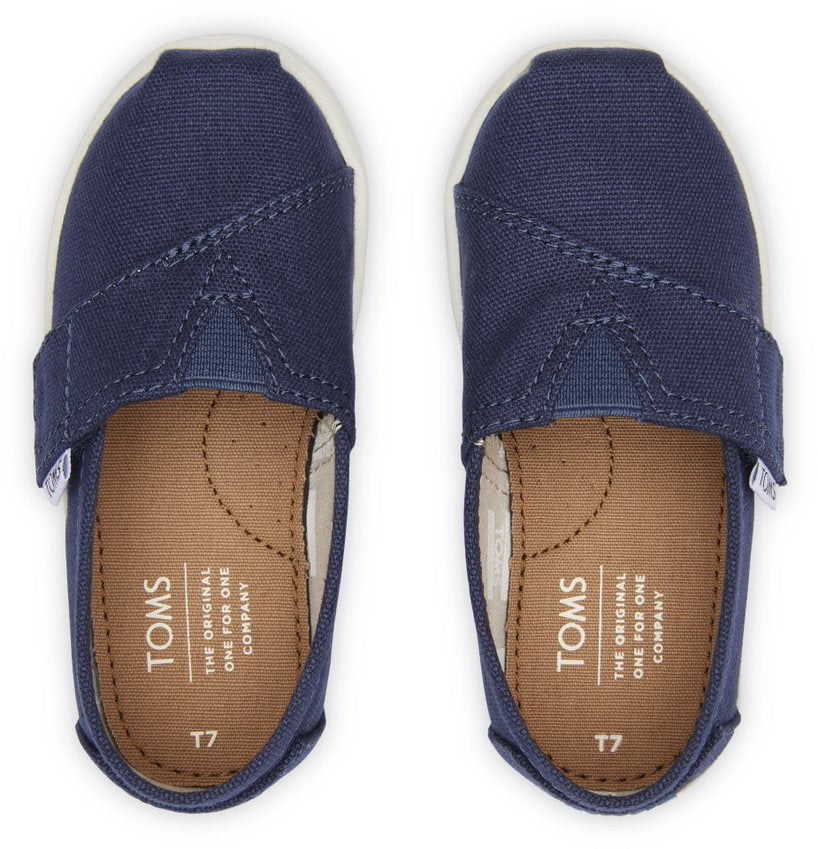 A unisex canvas shoe by TOMS, style Alpargata, in navy with a velcro strap. Top view of a pair.