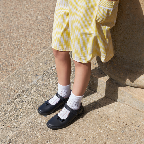 Girl wearing a pair of girls Mary Jane school shoes by Start Rite, style Giggle, in black leather with velcro fastening. Left side view.