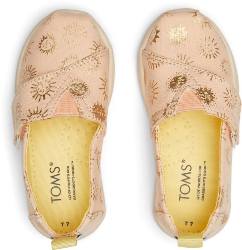 A girls canvas shoe by TOMS, style Alpargata Sunny Days, in apricot with gold foil detail and a velcro strap. Top view of a pair.