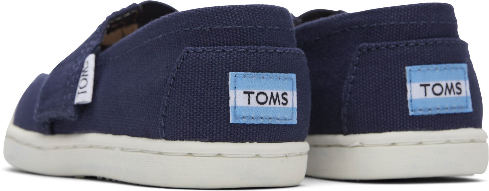 A unisex canvas shoe by TOMS, style Alpargata, in navy with a velcro strap. Back view of a pair.