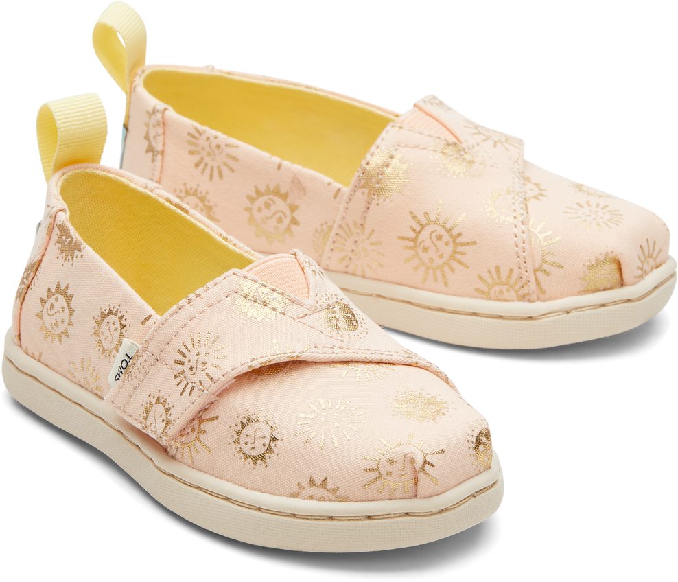 A girls canvas shoe by TOMS, style Alpargata Sunny Days, in apricot with gold foil detail and a velcro strap. Front view of a pair.