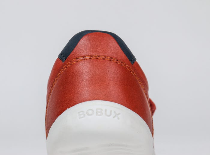 A boys smart trainer by Bobux,style Ryder, in orange and navy with velcro fastening. Back view.