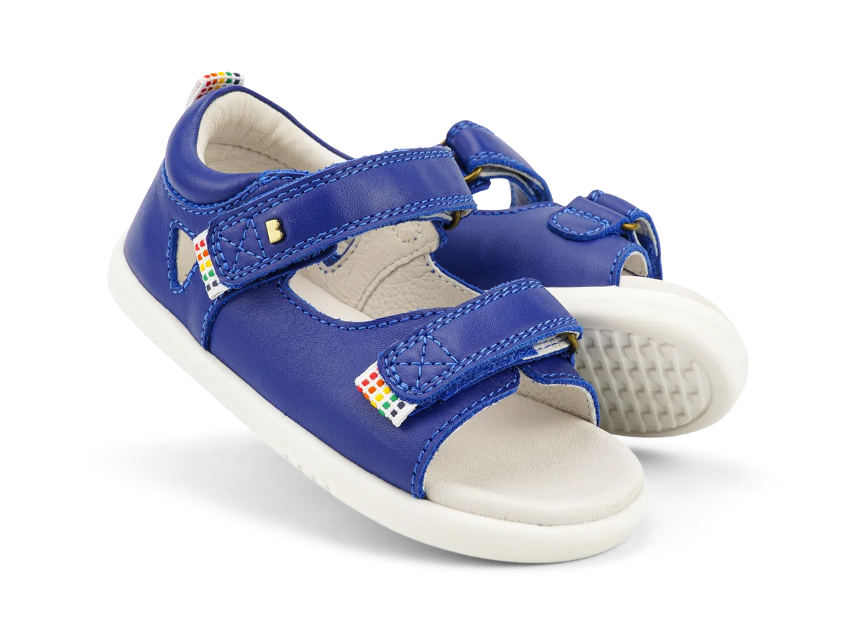 A pair of boys open toe sandals by Bobux, style Rise, in Blue leather with velcro fastening. Angled view.