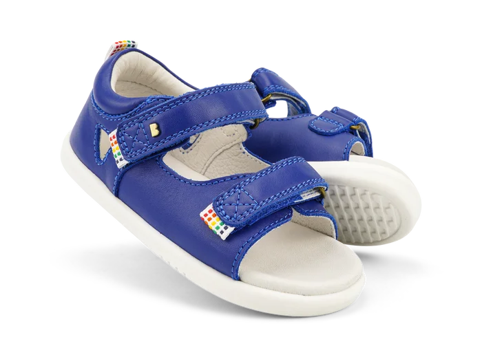 A pair of boys open toe sandals by Bobux, style Rise in Blue leather with velcro fastening. Angled view.