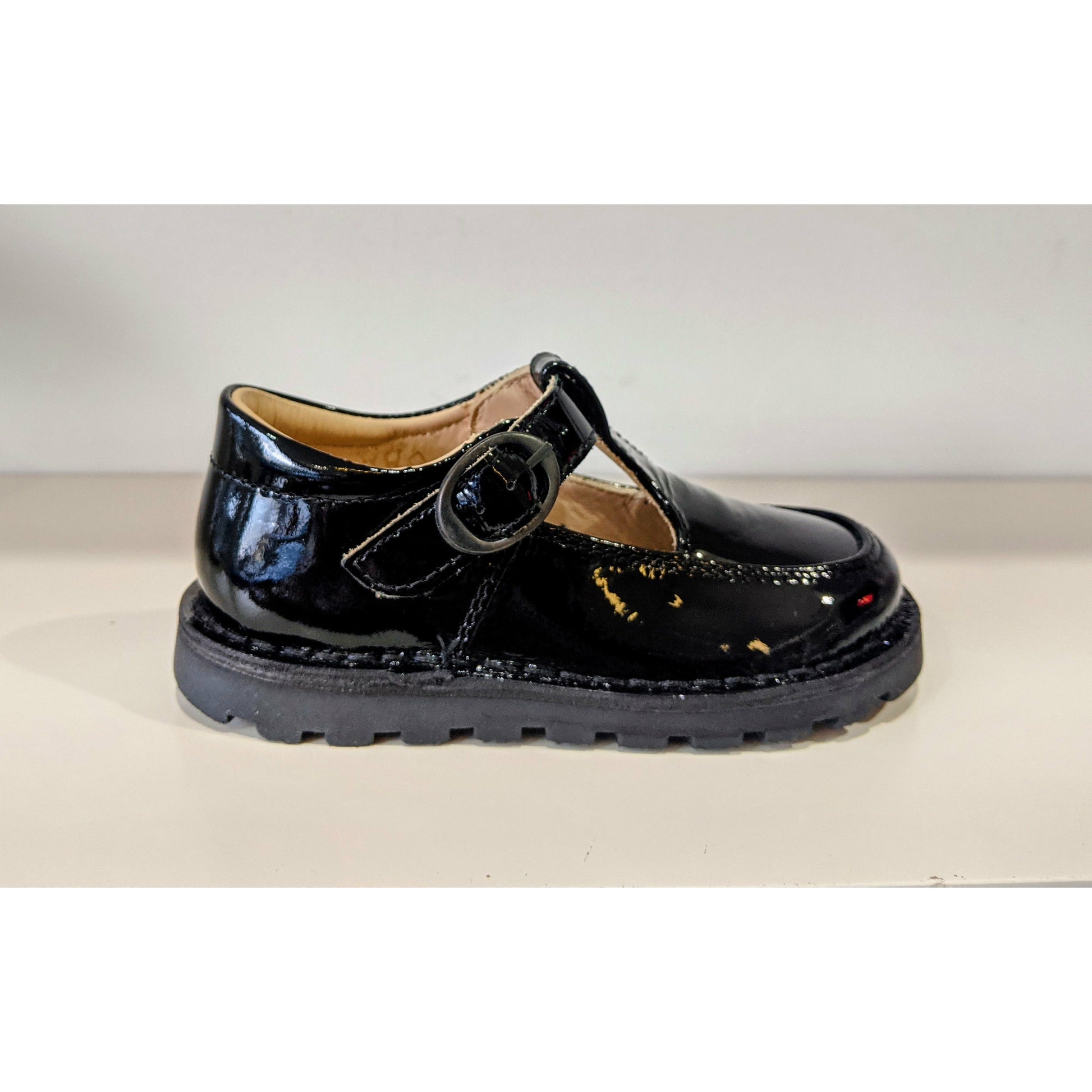 A girls T-Bar school shoe by Petasil, style Danny, in black patent with buckle fastening. Right side view.