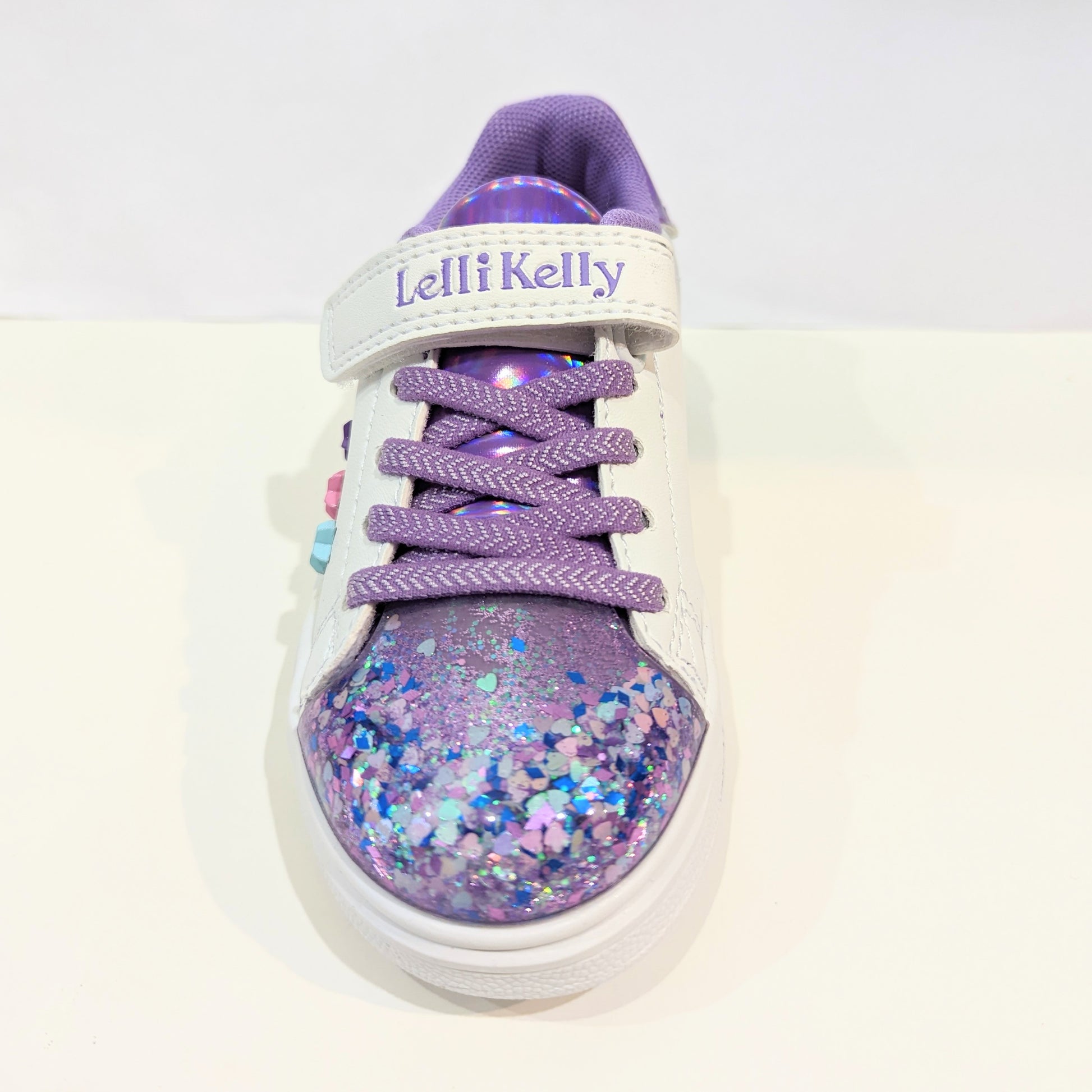 A girls casual trainer by Lelli Kelly, style Helene, in white and lilac leather with faux lace and velcro fastening. Front view.