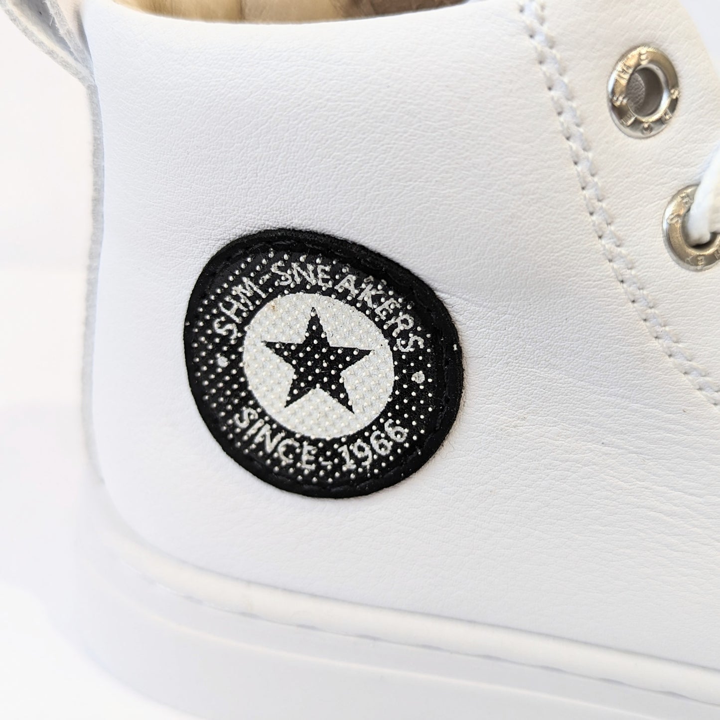 A unisex hi-top by Shoesme, Style SH21S008-F, in white with logo detail, lace/zip up. Close up of black and white logo with star at the centre.
