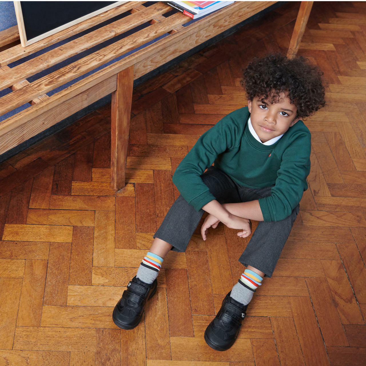 A boy sat down wearing a pair of boys school shoes by Start Rite,style Rocket, in black leather with double velcro fastening. Angled  view.