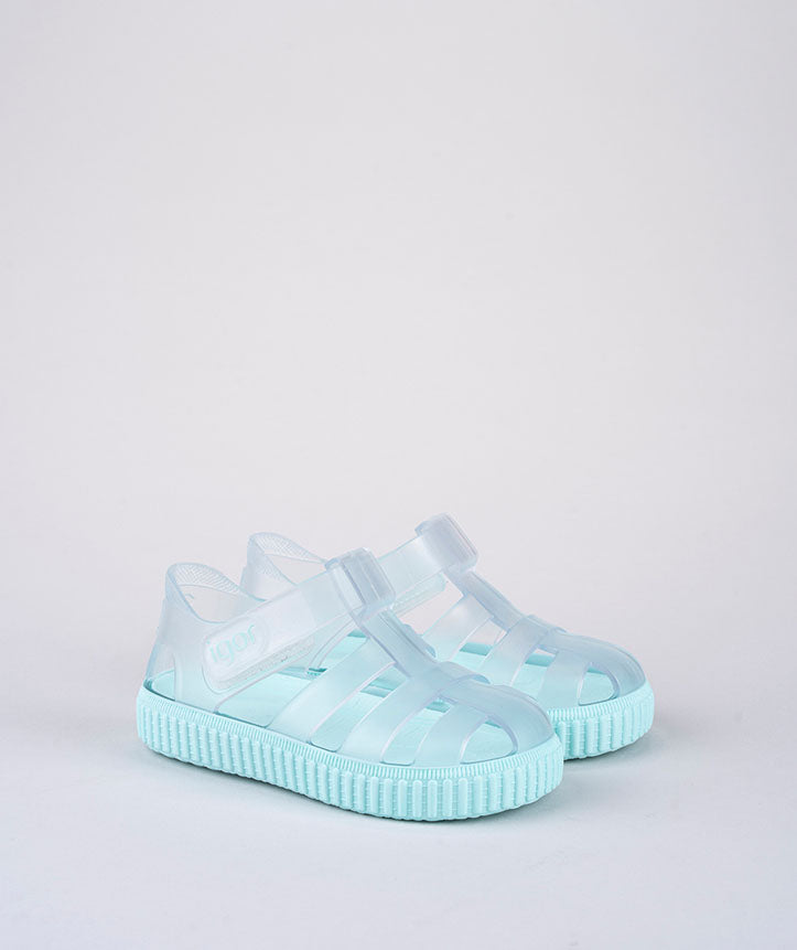 A pair of unisex closed toe sandals by Igor, style Nico, in clear and aqua with velcro fastening. Left side view.