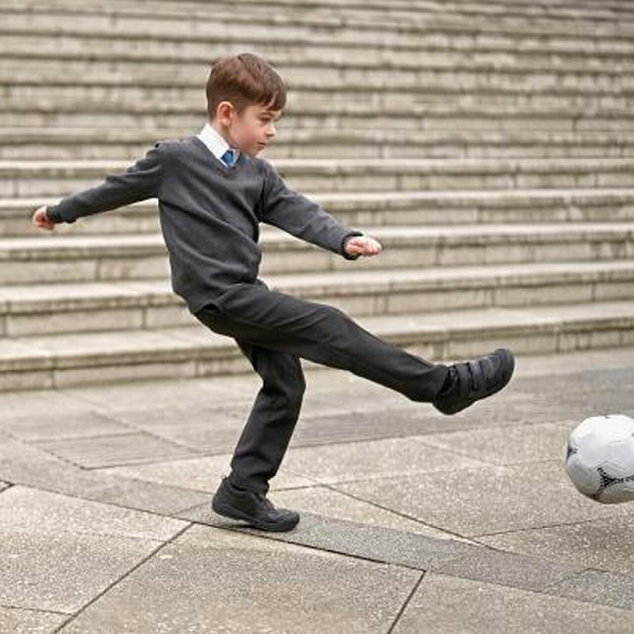 A boy wearing a pair of boys school shoes by Start Rite, style Strike, in black leather with double velcro fastening. Right side view.