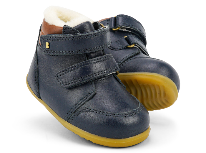 A pair of boys waterproof fur lined ankle boots by Bobux, style Timber Arctic, in Navy and tan leather with double velcro fastening. Angled view.