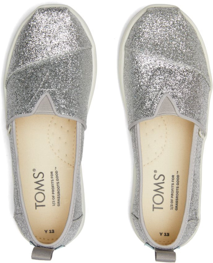 A girls canvas shoe by TOMS, style Alpargata, a slip on in silver glitter. Top view of a pair.