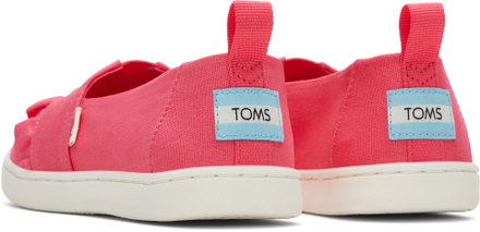 A girls canvas shoe by TOMS, style Alpargata Bow in the colour Pink Raspberry with a velcro fastening. Rear view of a pair.