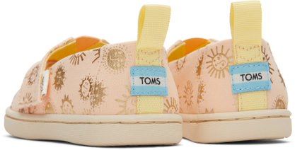 A girls canvas shoe by TOMS, style Alpargata Sunny Days, in apricot with gold foil detail and a velcro strap. Back view of a pair.